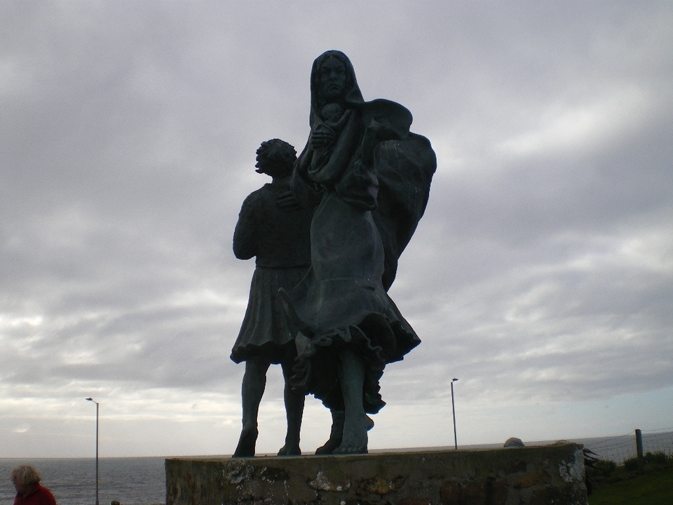 A statue of two figures under a cloudy sky.