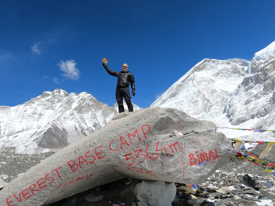 A person standing proudly at Everest Base Camp with mountains behind.