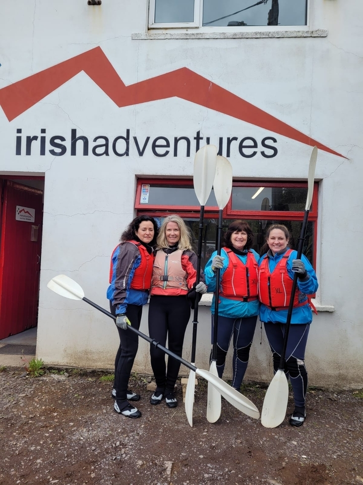 Quatre personnes en gilets de sauvetage tenant des pagaies devant un bâtiment.