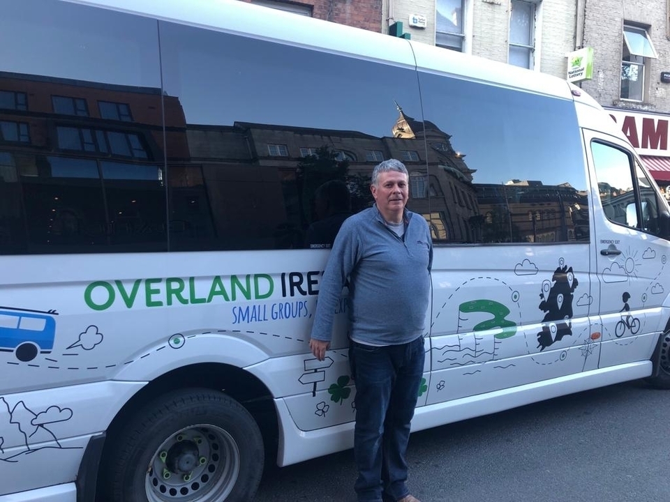 Homme debout à côté d'un van de tourisme en Irlande.