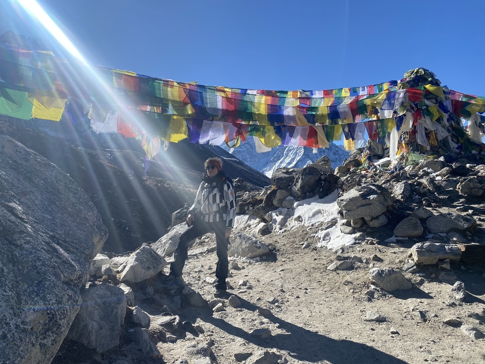 Person standing next to prayer flags and mountains.