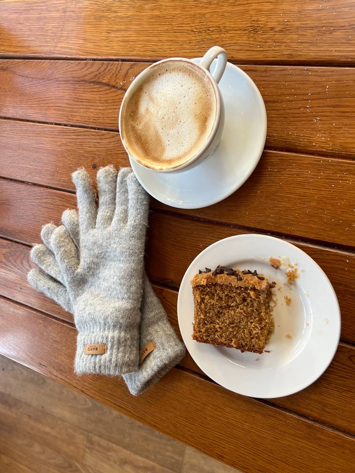 Cup of coffee with a slice of cake and gloves.