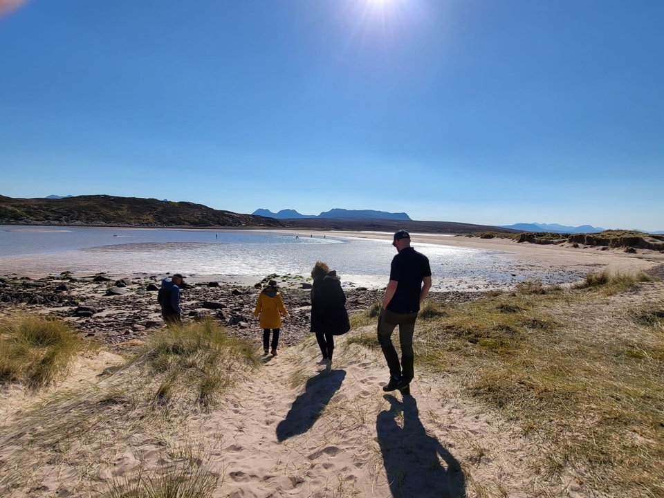 Des gens qui marchent sur une plage de sable avec des collines en arrière-plan.