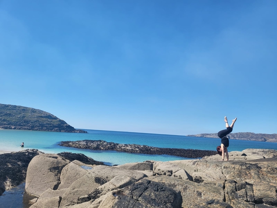 Personne faisant le poirier sur des rochers près d'une eau turquoise claire
