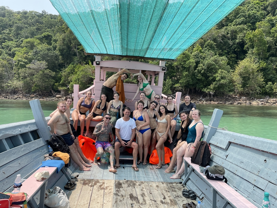 Group of people on a boat in clear water with forest in the background.