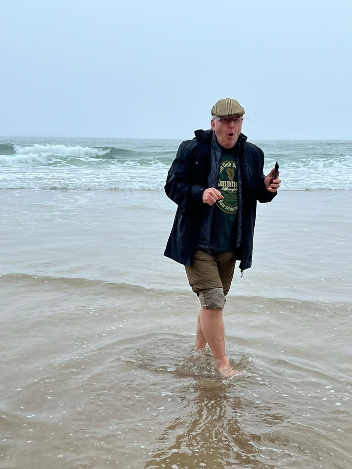 Homme marchant sur une plage avec des vagues en arrière-plan.