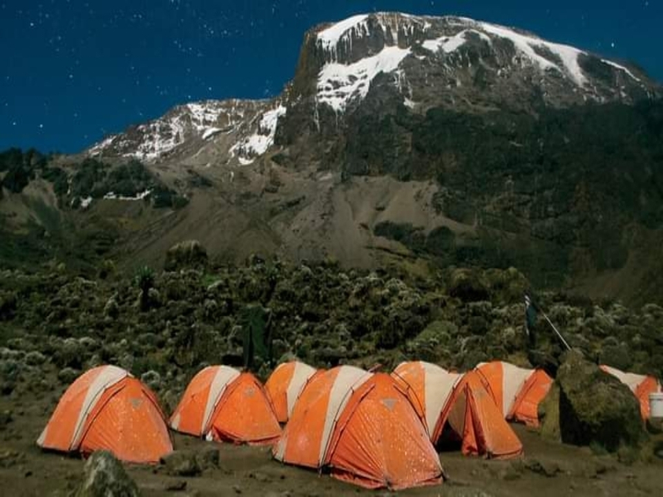 Vue nocturne d'un camping avec des tentes sous la montagne.