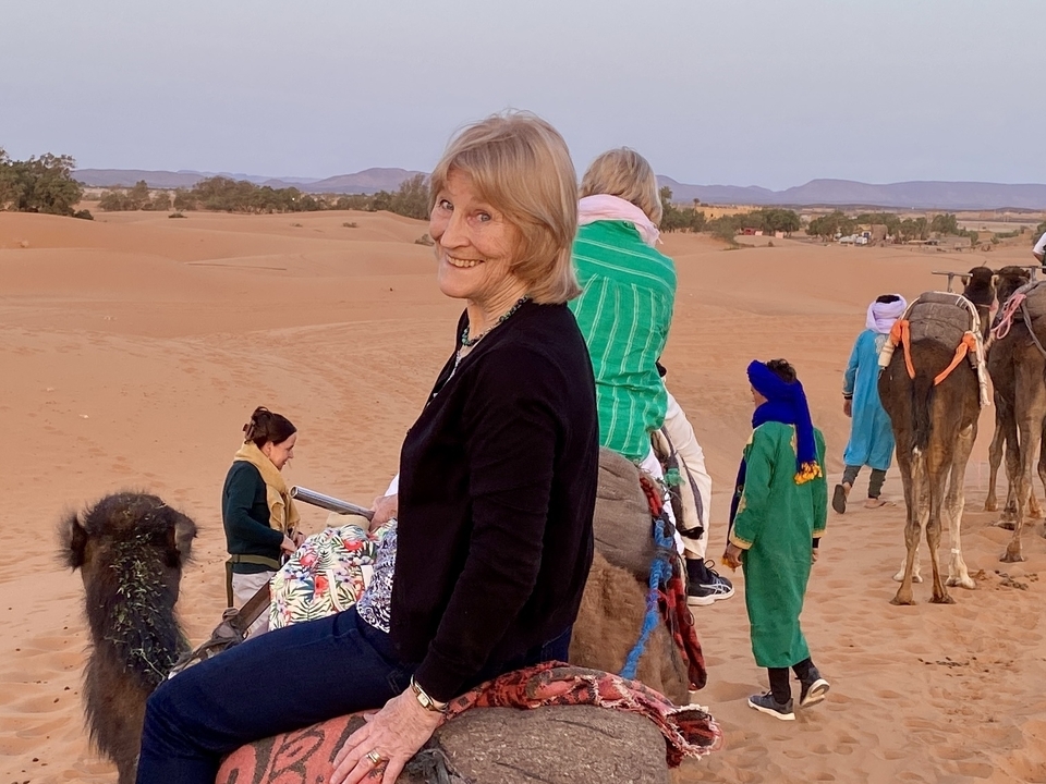 Group of people riding camels in a desert landscape.