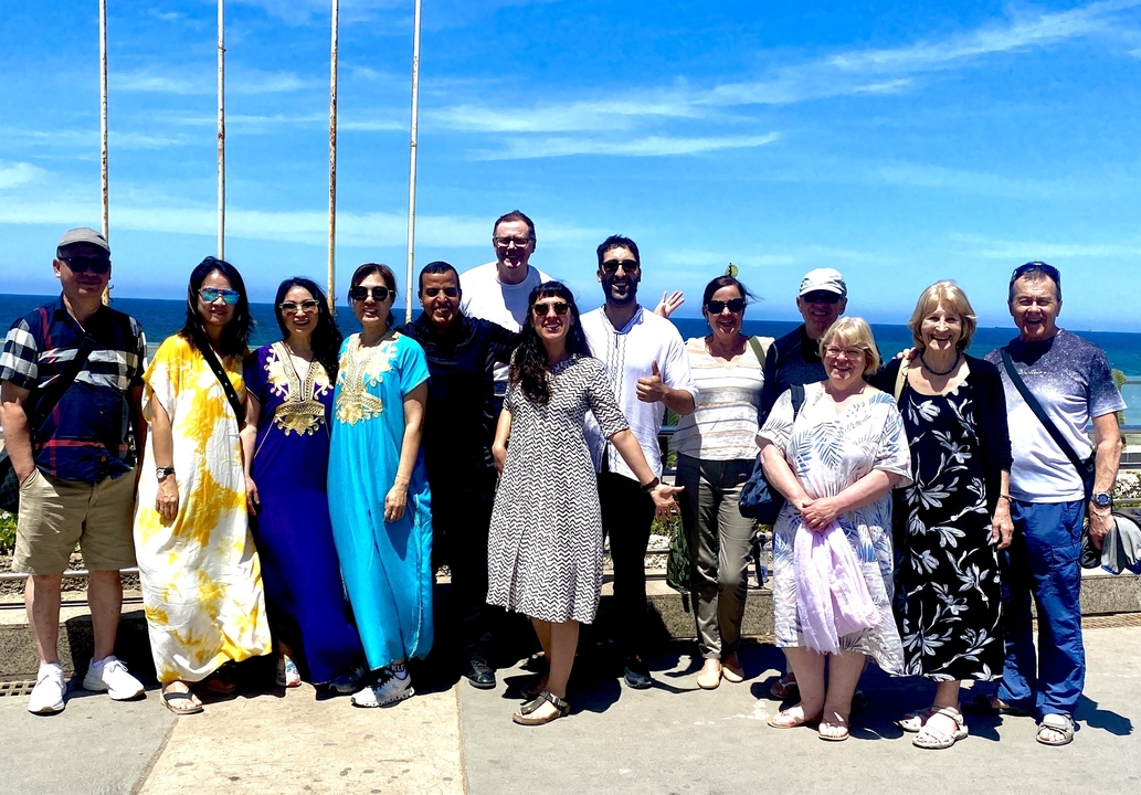 Group of tourists in colorful attire posing with a view of the ocean.