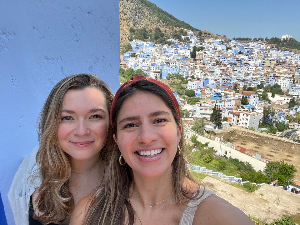 Two people smiling with a background of blue-painted buildings.