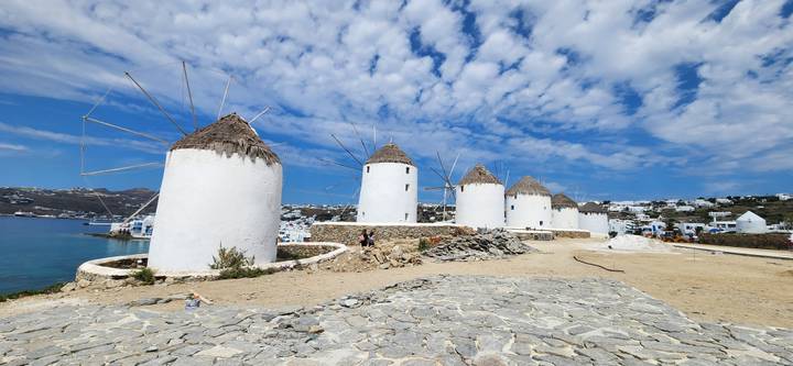Iconic windmills against a blue sky with a view of Mykonos.