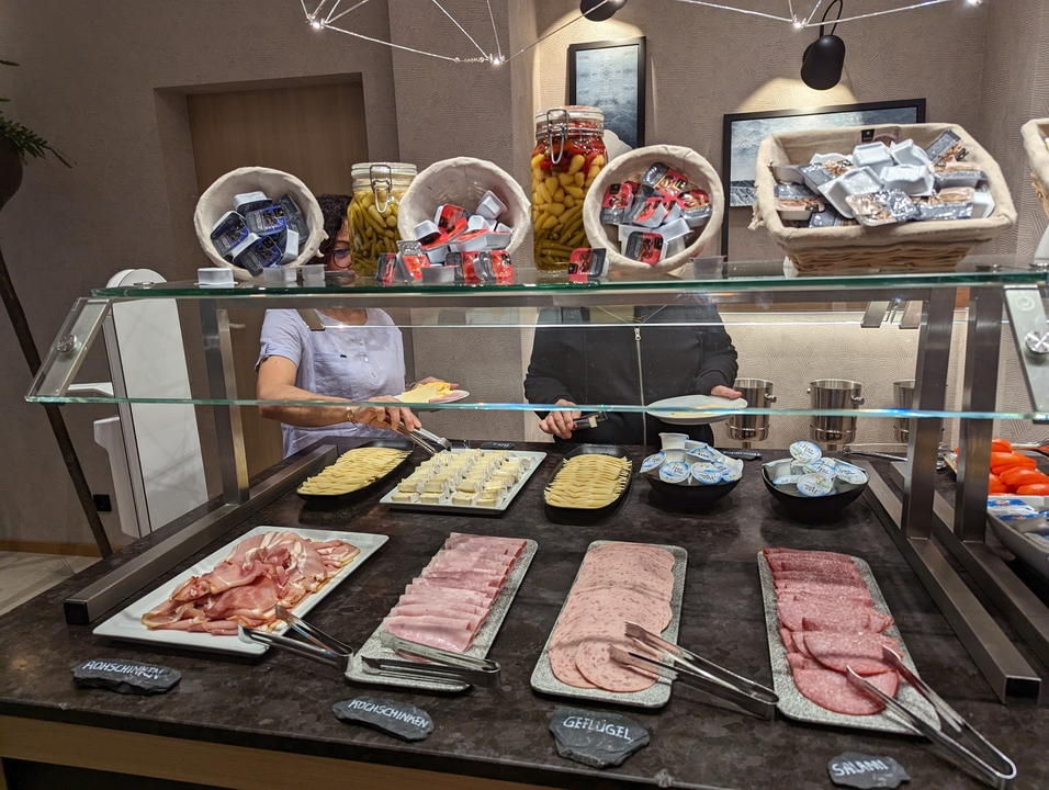 Une table de buffet présentant diverses viandes et fromages avec des personnes qui se servent.