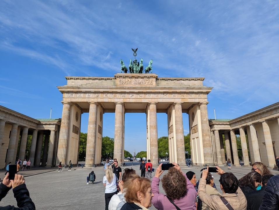 Grande porte historique avec des sculptures au sommet, entourée de touristes.