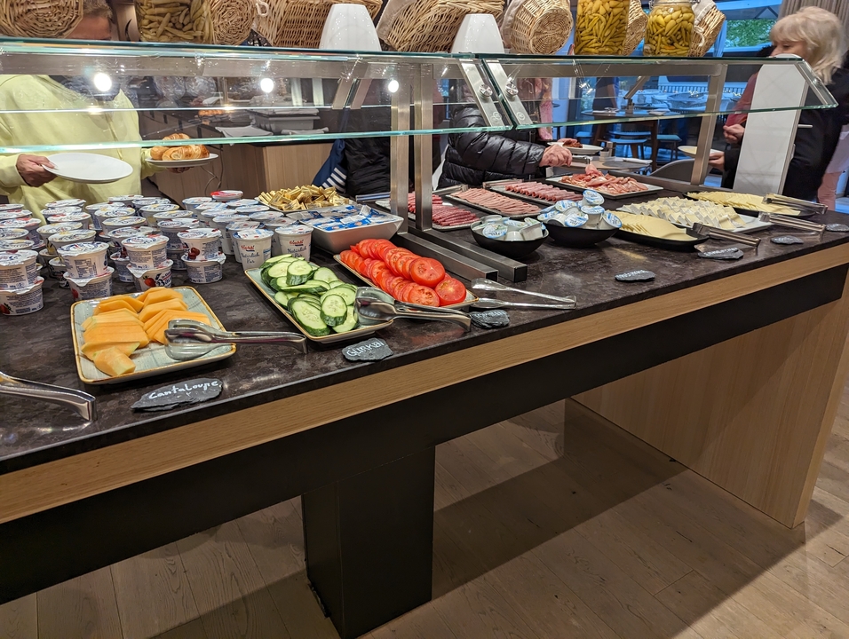 Une table de buffet avec de la charcuterie assortie, du yaourt et des légumes tranchés.