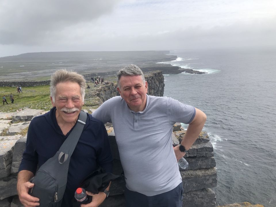 Two men standing on a cliff with ocean views.