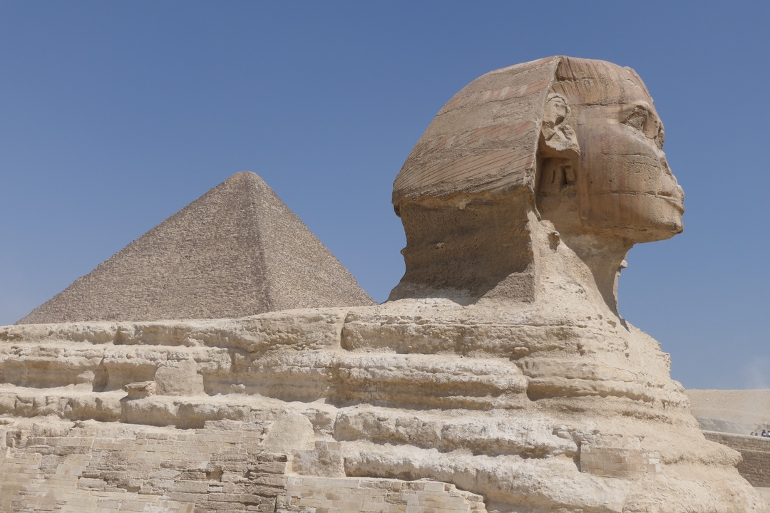 The Sphinx and a pyramid under a clear blue sky in Egypt.