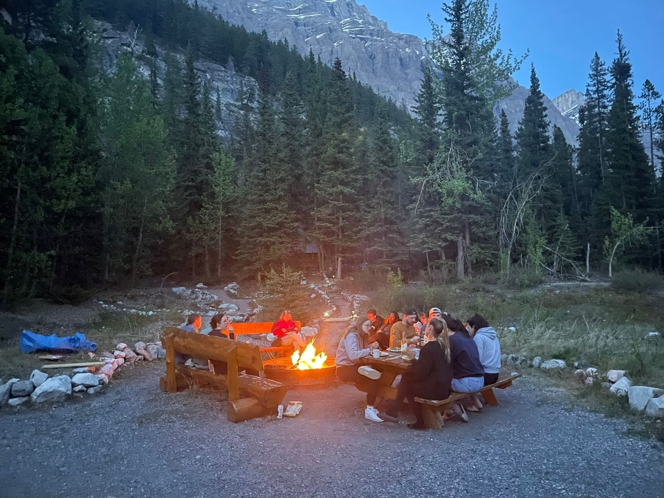 Group of people around a campfire in the woods at twilight.
