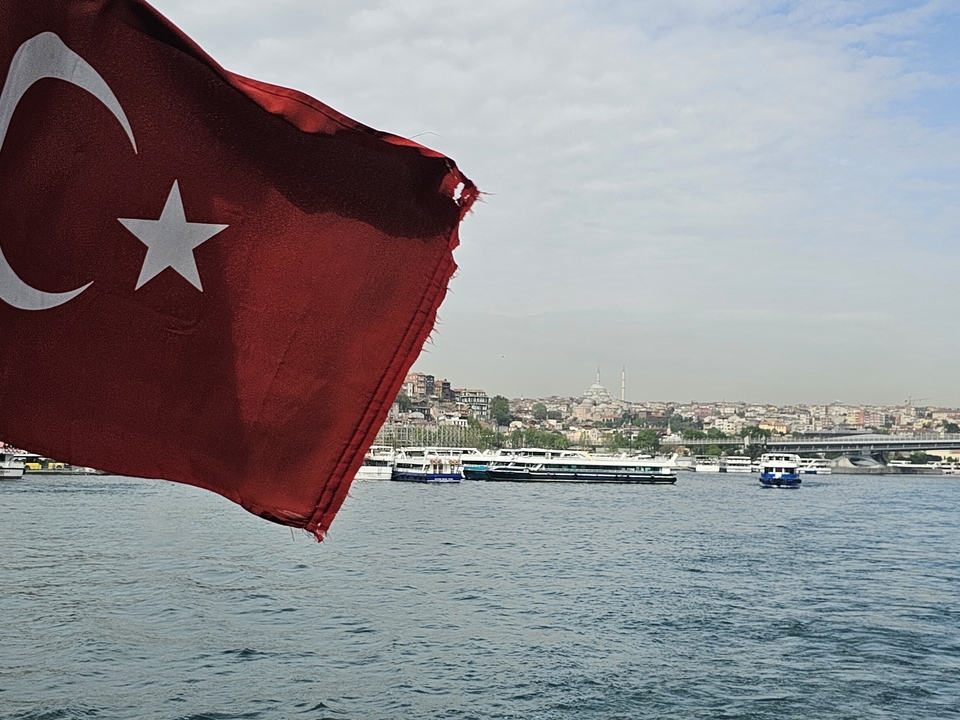 Drapeau turc flottant sur un bateau avec un paysage urbain en arrière-plan.