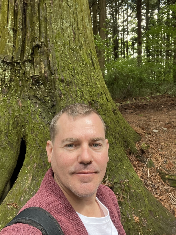 Personne se tenant debout à côté d'un gros tronc d'arbre.