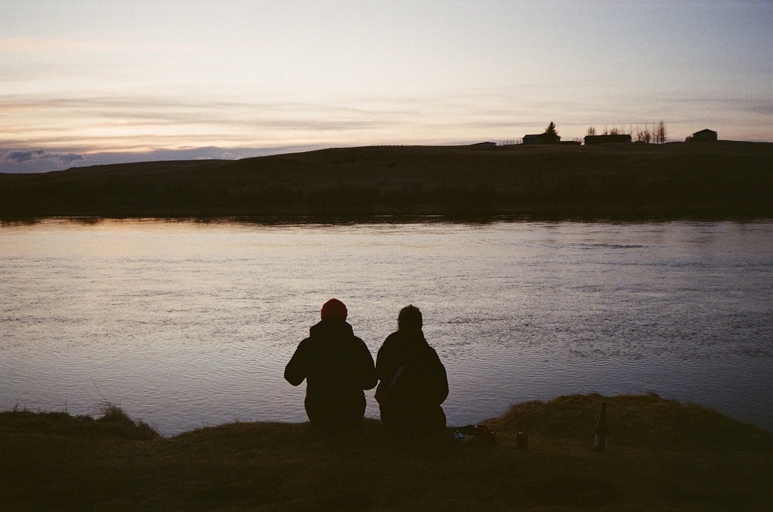 Two people sitting by a river at sunset.