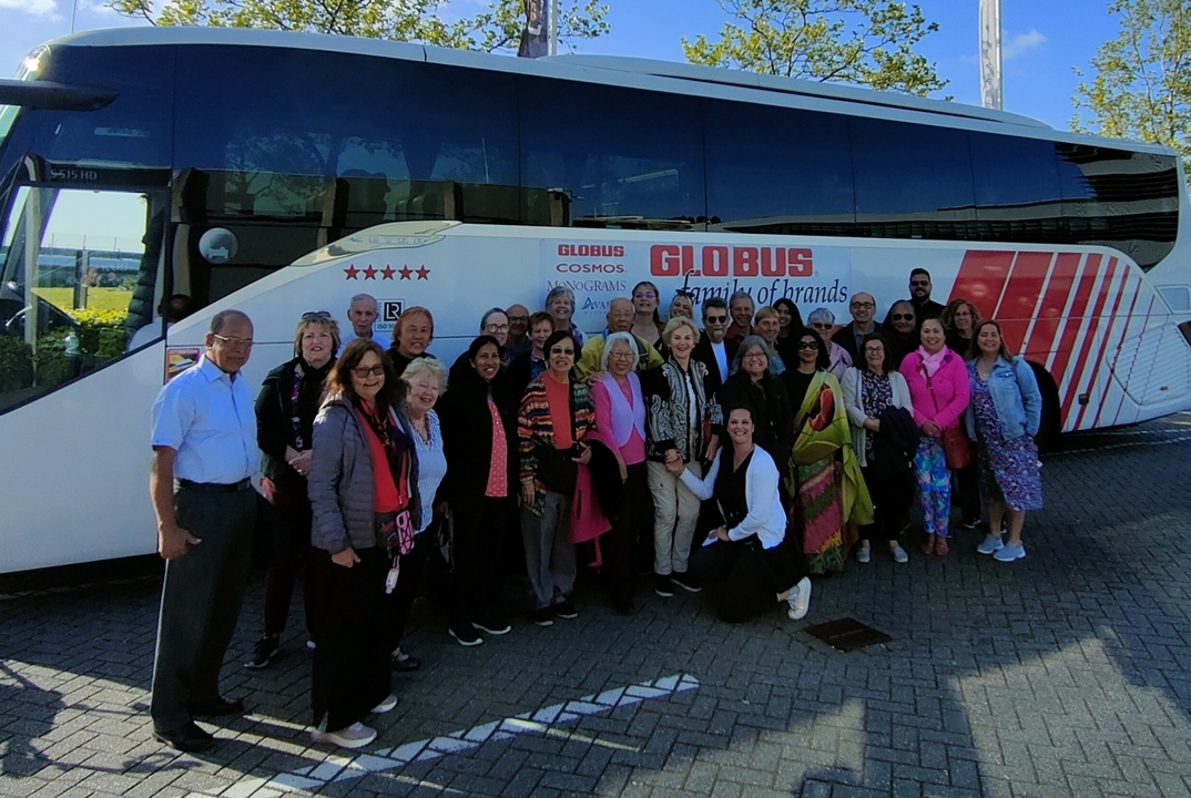 Photo de groupe devant un autocar de tourisme dans une zone pavée.