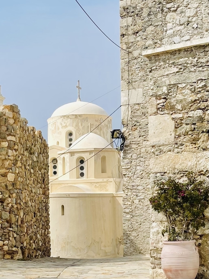 White church with domes behind a stone wall.