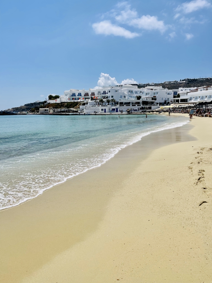 Sandy beach with clear waters and white buildings in the background.