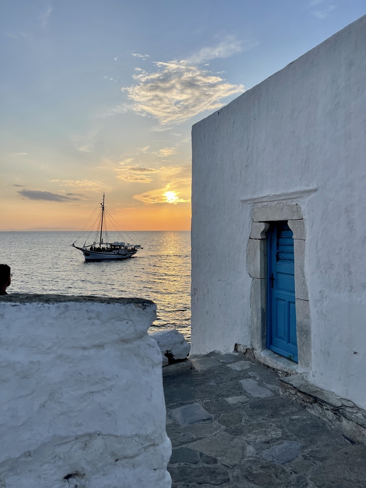 Sailing boat on the sea during sunset with a stone building nearby.
