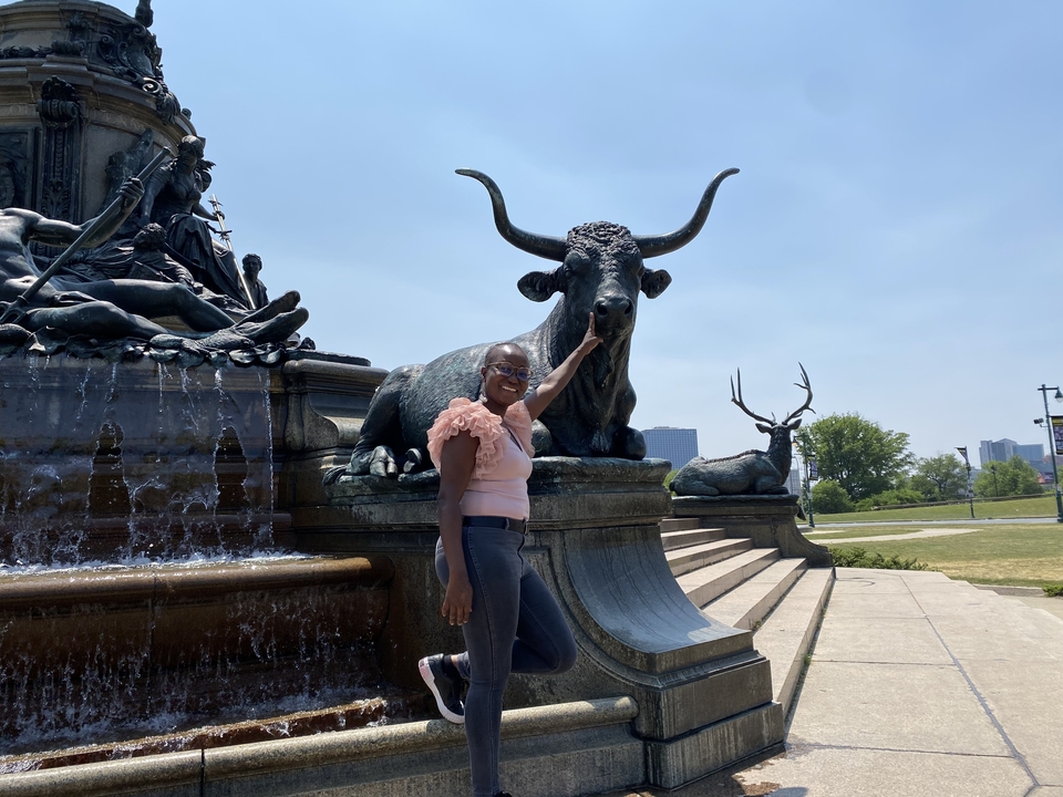 Person posing with a fountain sculpture.