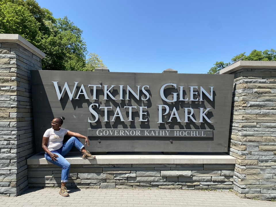 Person sitting in front of the Watkins Glen State Park sign.