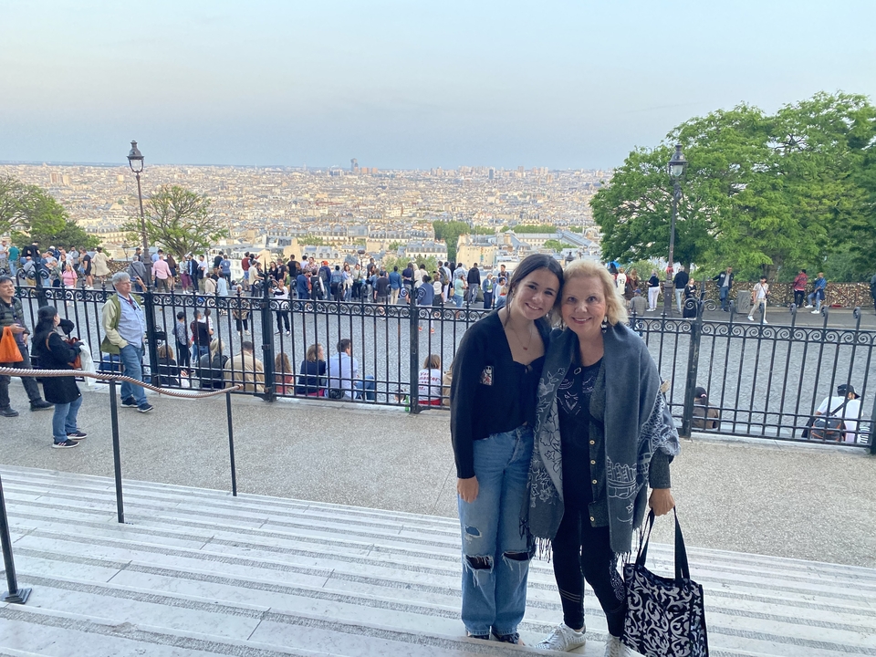 Two people posing with a panoramic view of a city from an elevation.