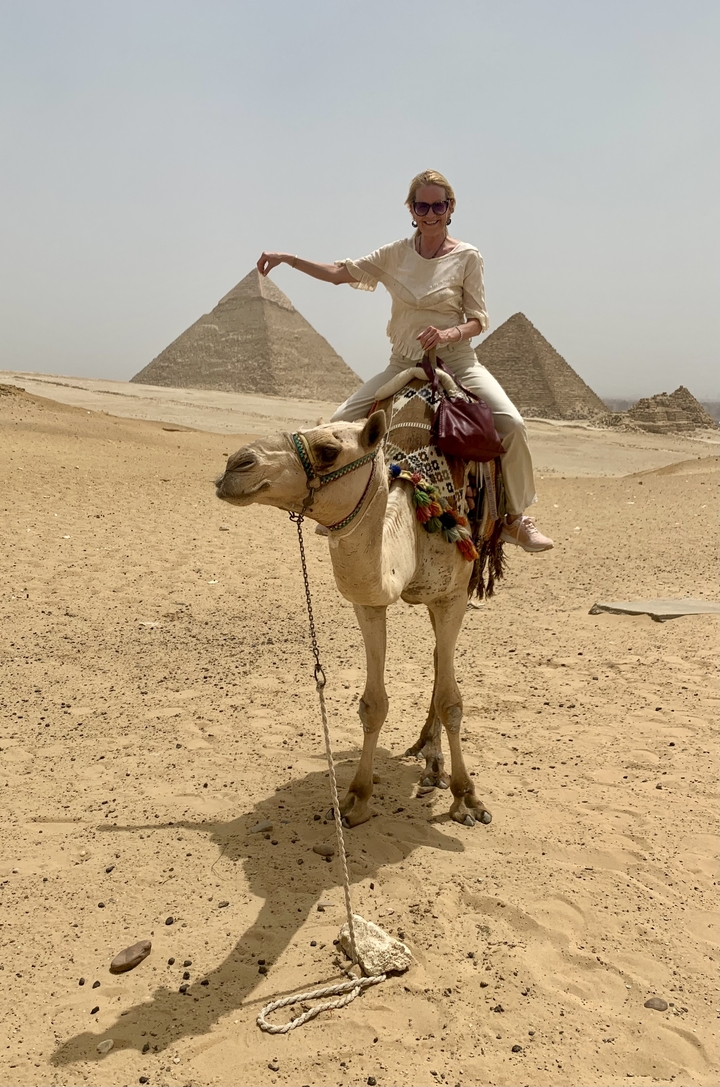 Person on a camel with a view of pyramids in the background.