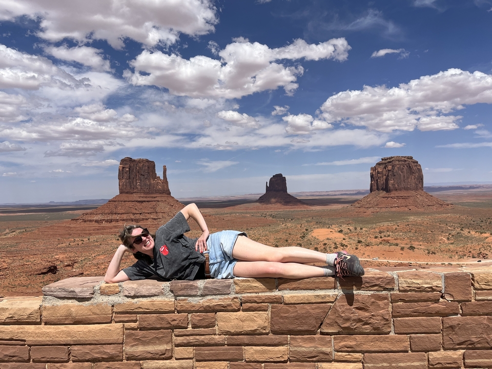 Person posing on a wall with Monument Valley in the background.