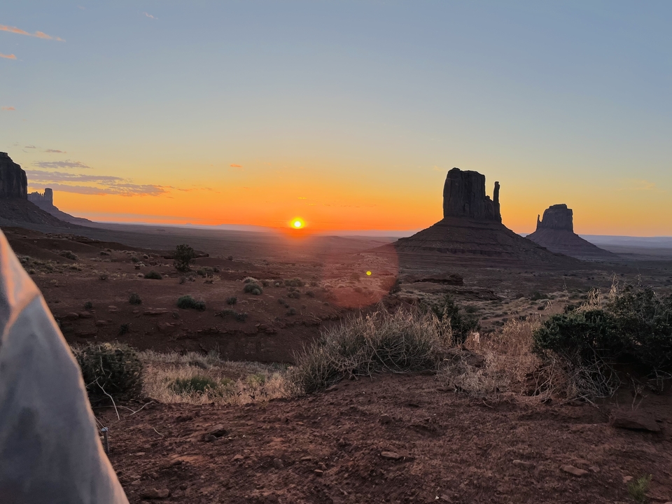 Sun setting behind Monument Valley with red rock formations.