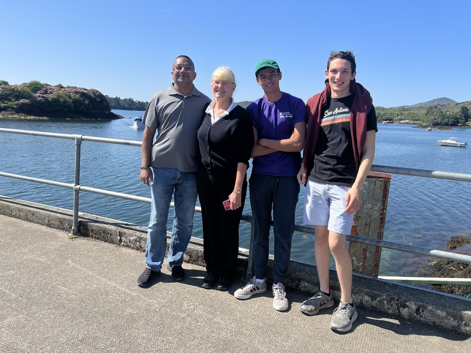 Group of people standing by a railing with a scenic view of water and hills.