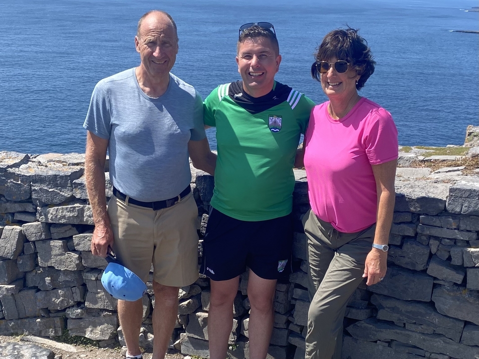 Group of three people standing on a stone wall by the ocean.