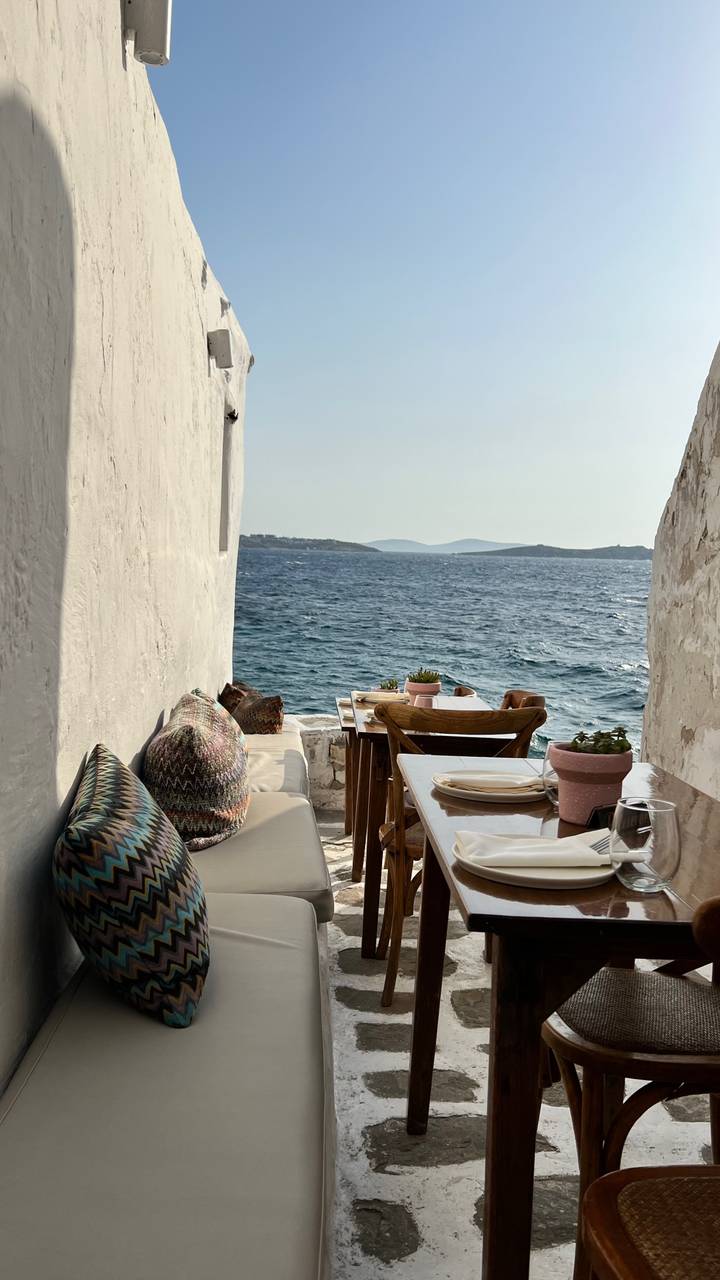 Outdoor dining area by the sea with cushions and wooden furniture.