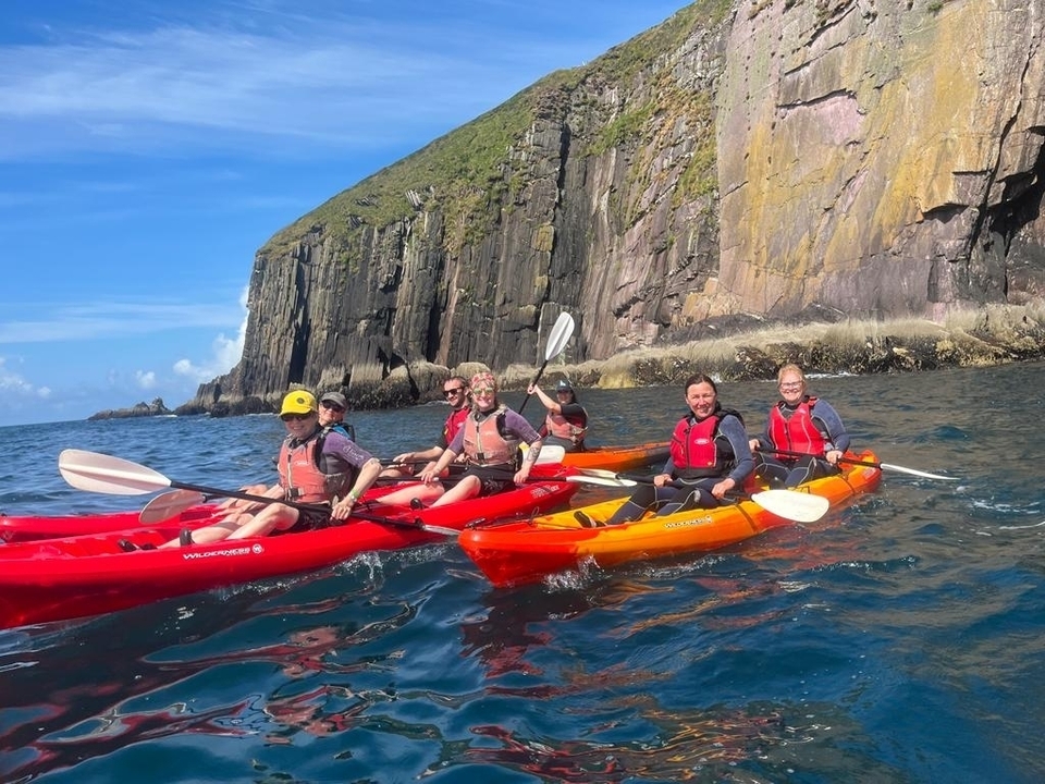 Group kayaking near a rocky cliffside.
