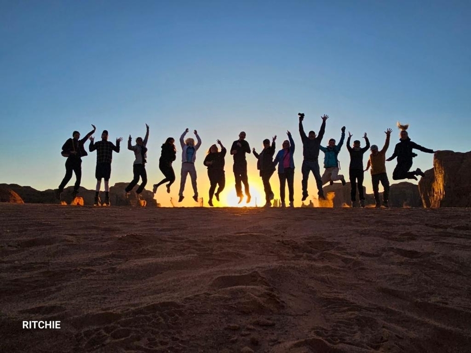 Groupe de personnes sautant au coucher du soleil dans un paysage désertique.