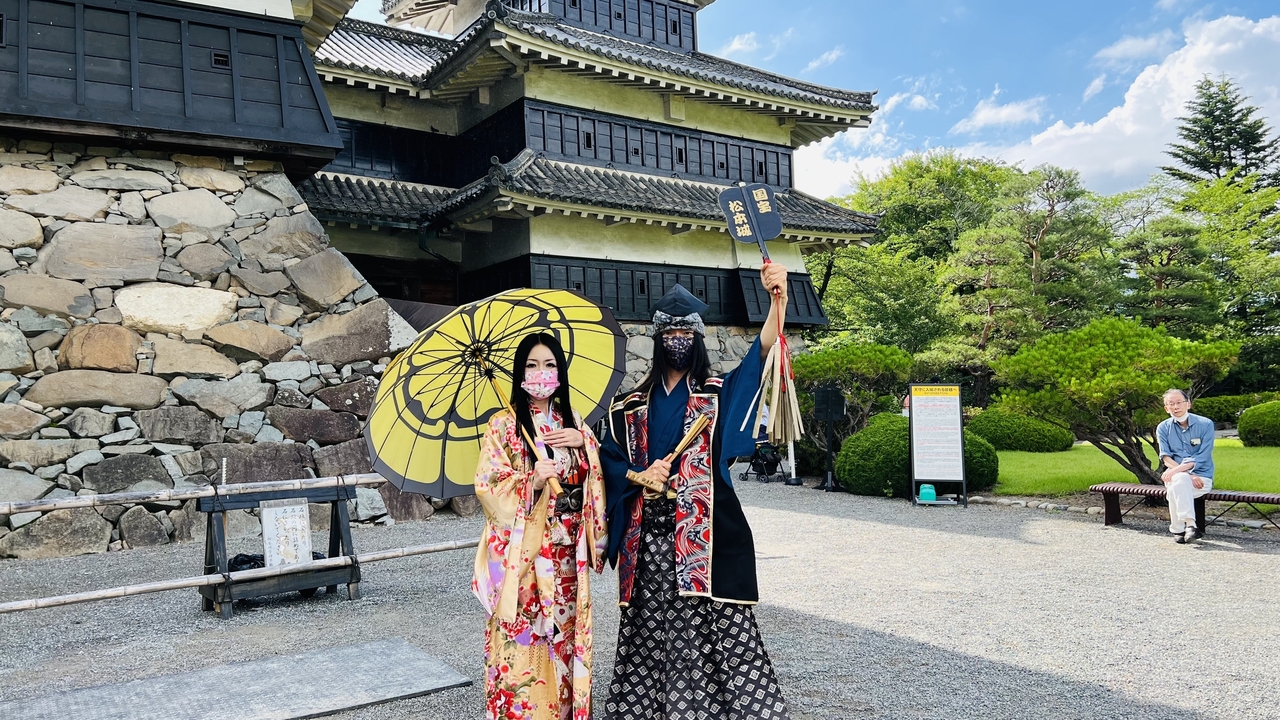 Two people in traditional attire in front of a historic Japanese castle.