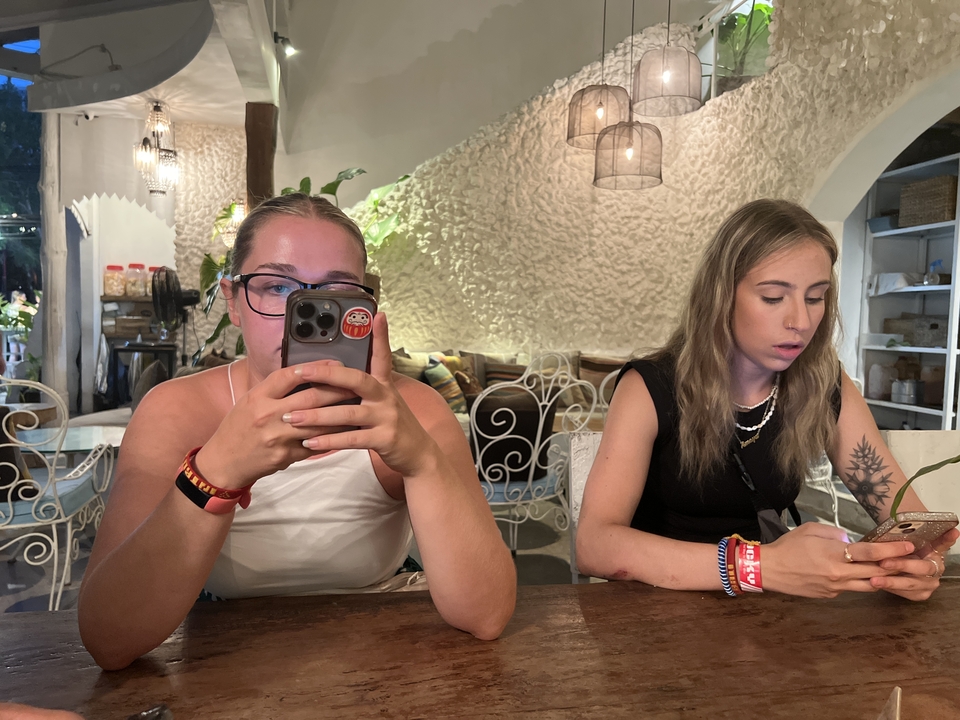 Two women sitting indoors, engaged with their phones.