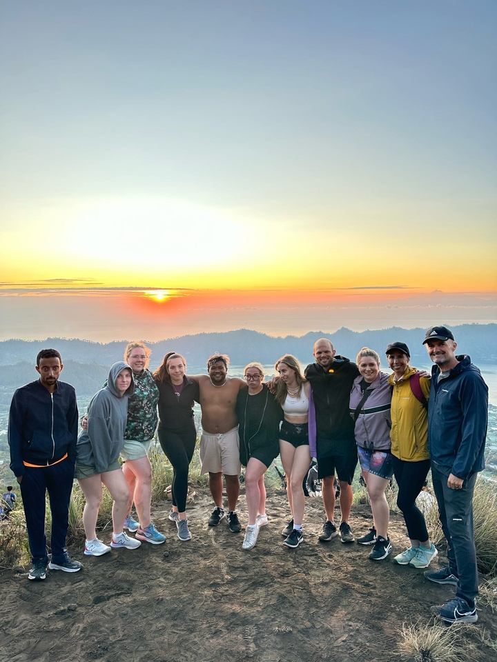 Group smiling and posing at sunrise with a scenic view.
