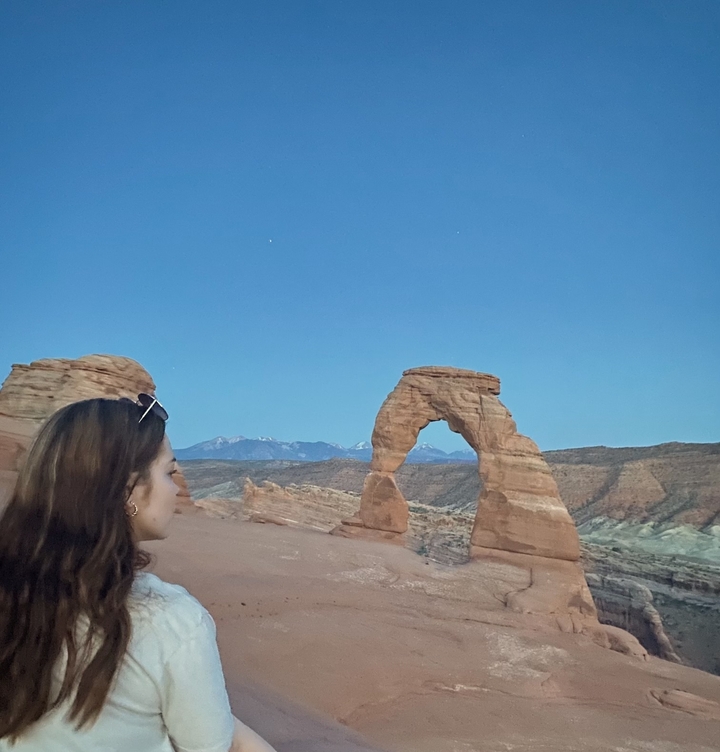 Person standing near Delicate Arch at twilight.