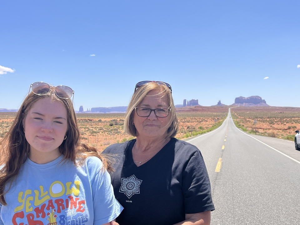 Two people standing on a road with Monument Valley in the distance.