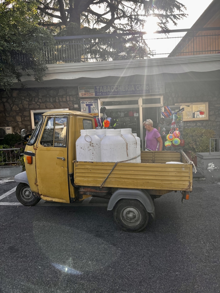 Yellow utility vehicle carrying large white containers on a street.