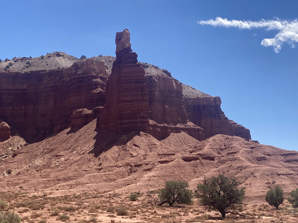 Tall rock formation in a red sandstone landscape under a clear blue sky.