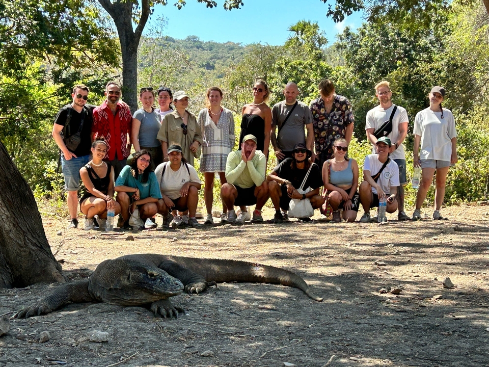 A large group of people behind a Komodo dragon in a forest setting.