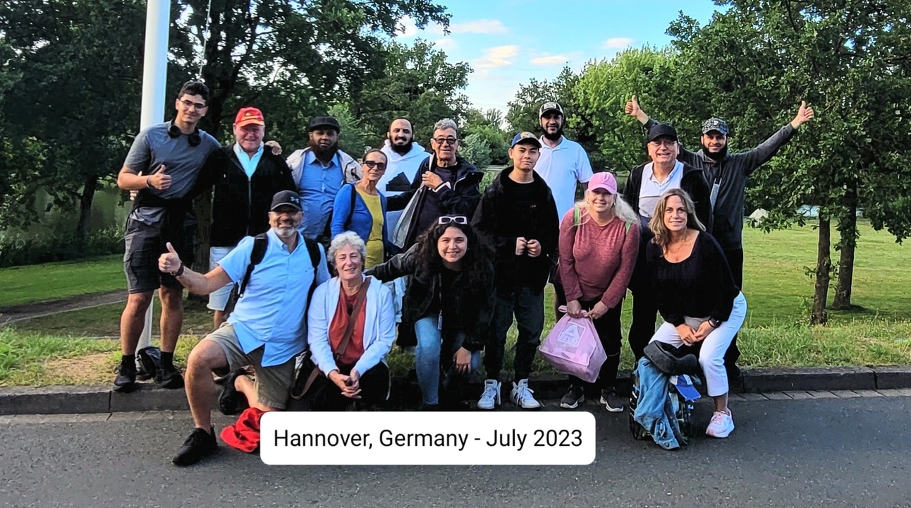 Un groupe de touristes posant à l'extérieur avec un texte superposé indiquant le lieu et la date.