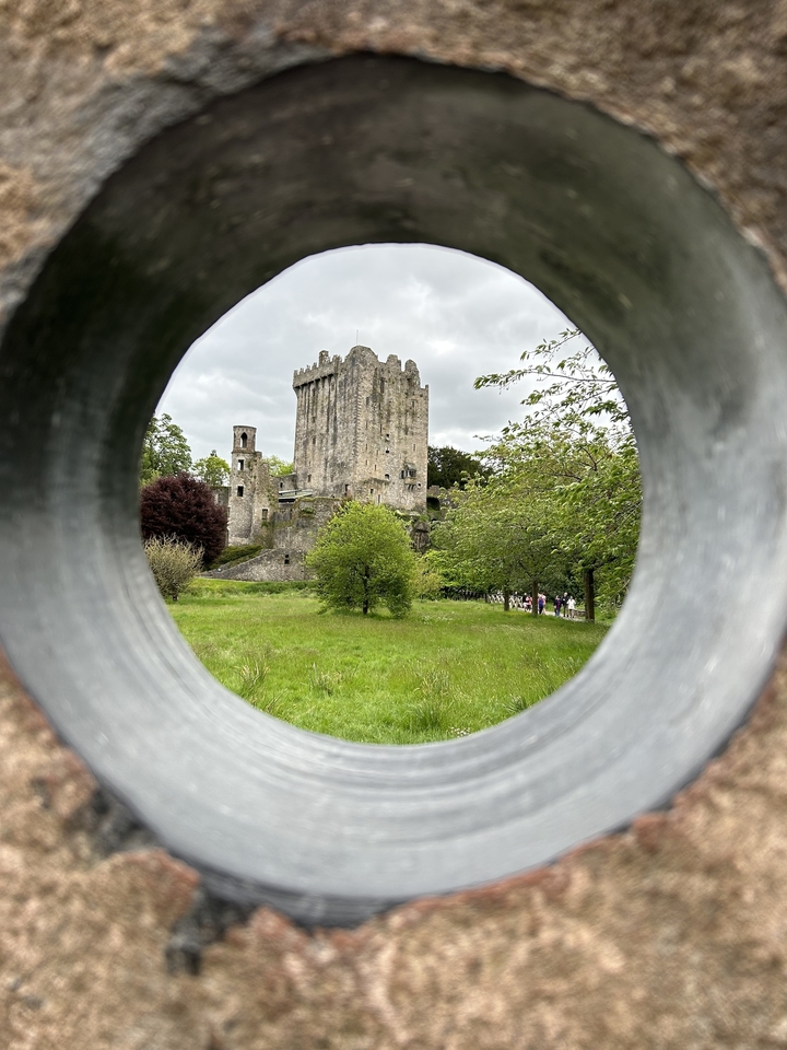 Château de Blarney encadré par des arbres et une ouverture circulaire dans la roche.