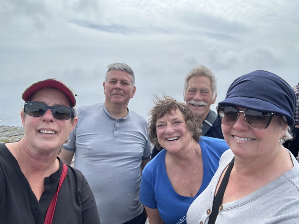 Un groupe de cinq personnes souriantes pour un selfie par temps nuageux.